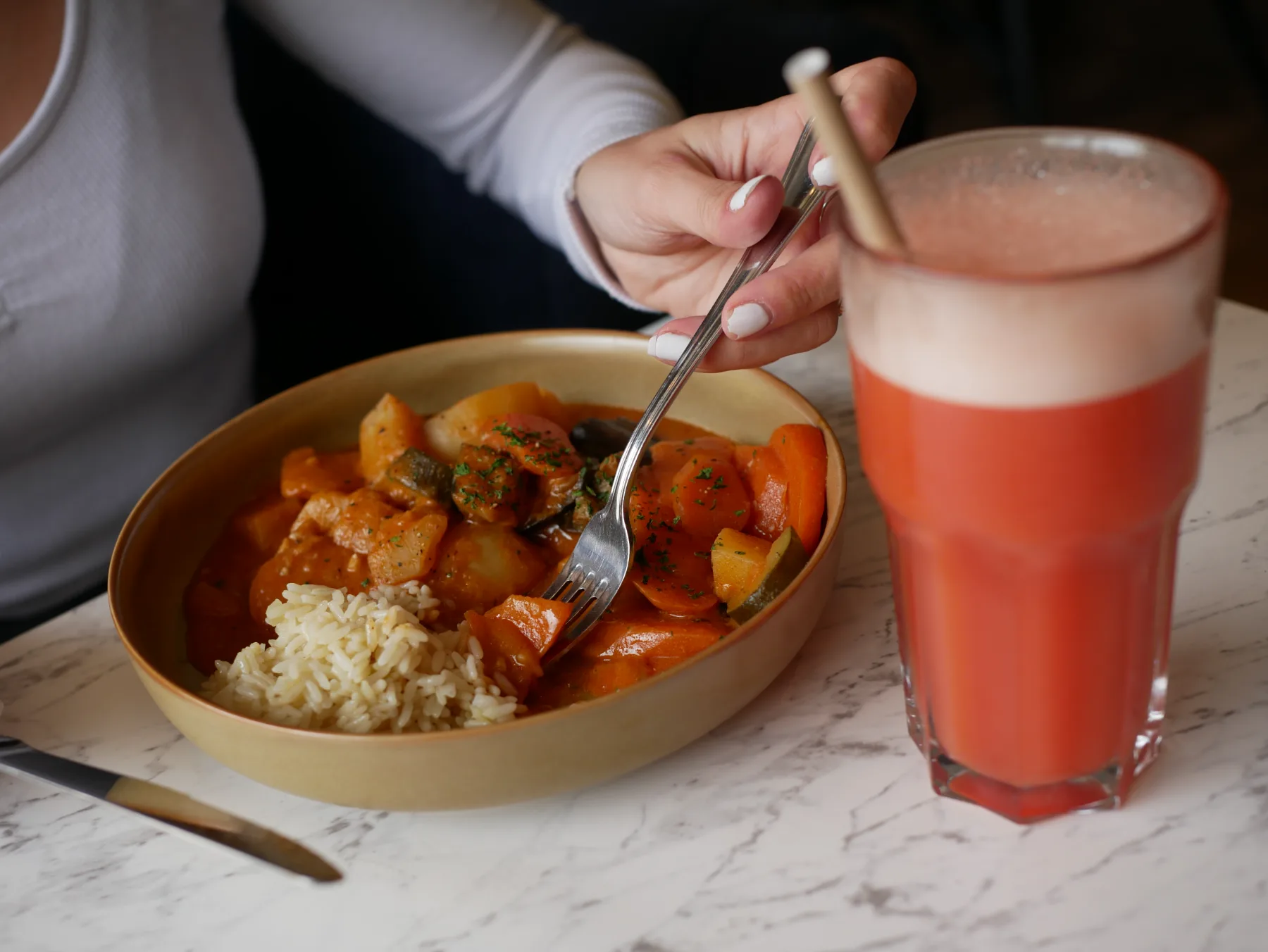 Plat mijoté aux légumes et riz servi dans un bol, accompagné d’une limonade rouge, sur une table de marbre.