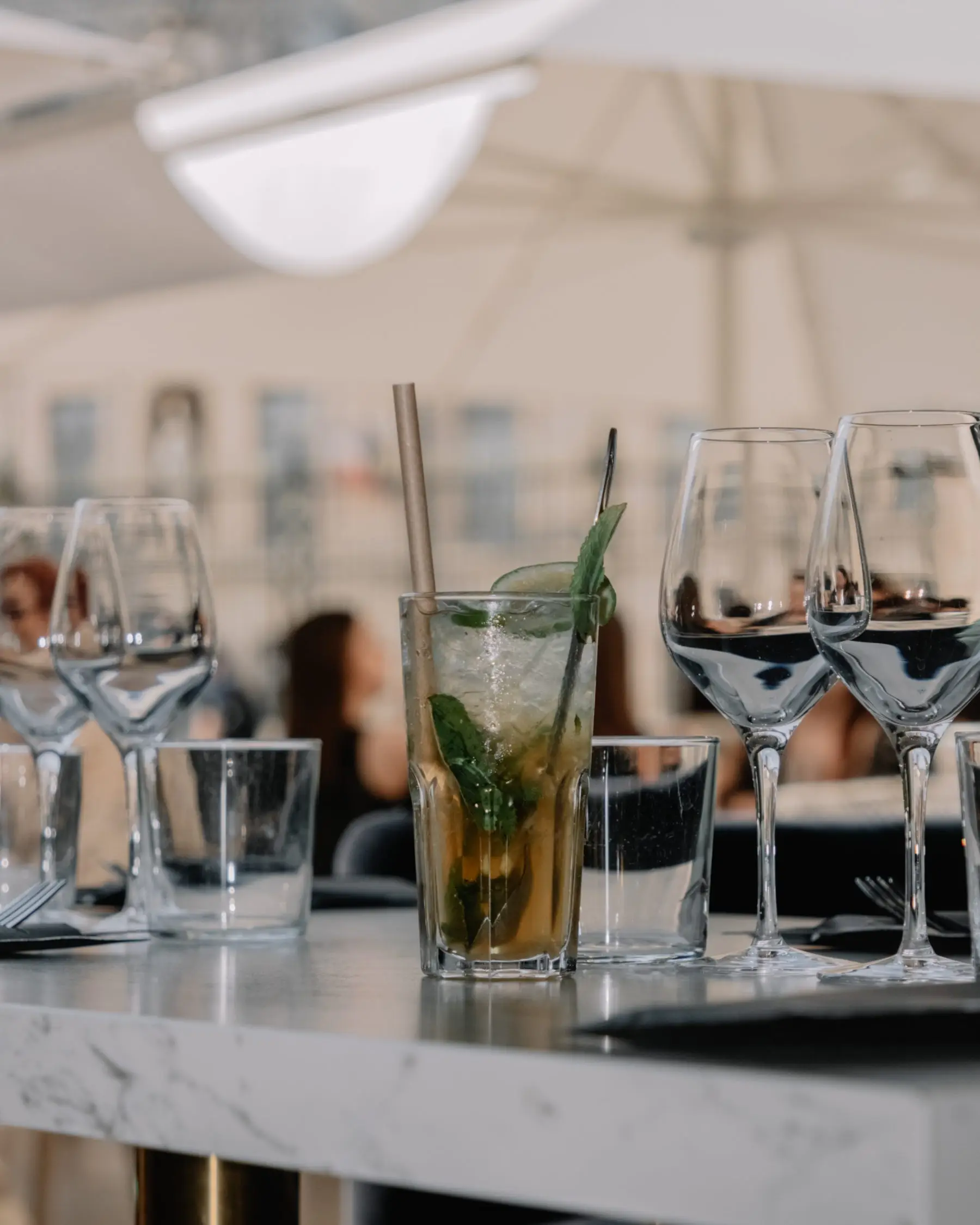 Verres à vin et mojito sur une table de marbre, en terrasse sous les parasols.